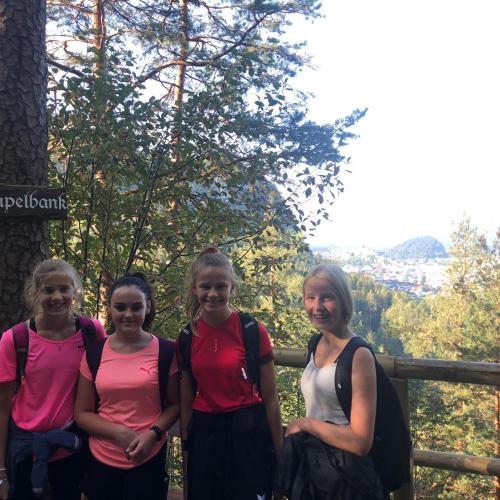 vier Mädchen stehen vor einem Holzzaun, Bäume im Hintergrund